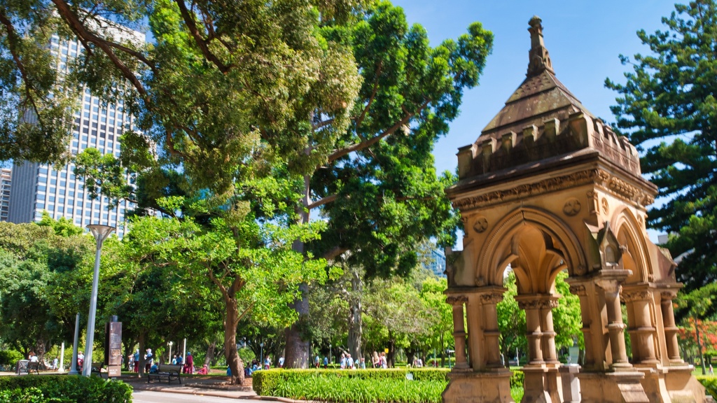 An image of Hyde Park with an architectural structure in the park with buildings and people in the background