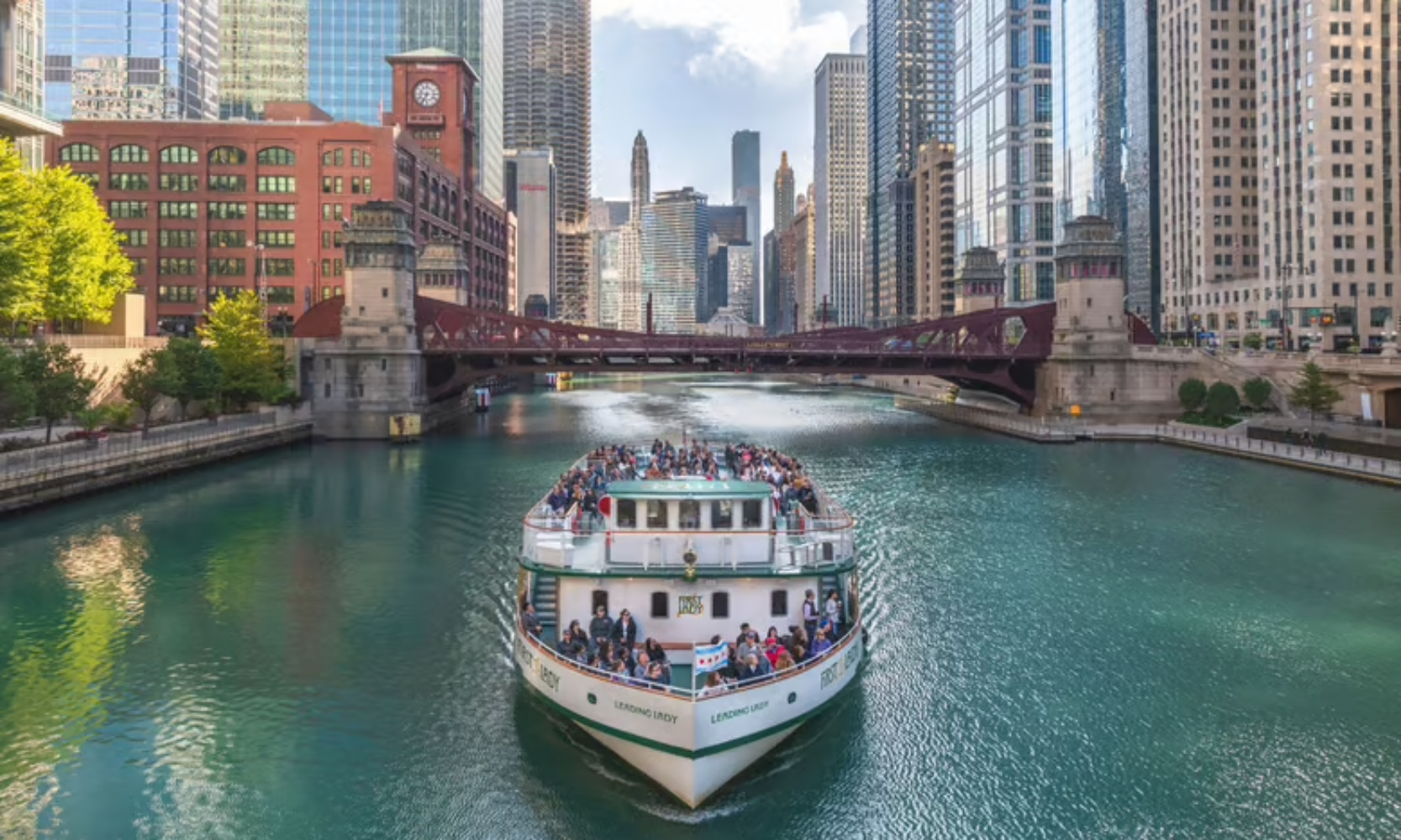 Front view image of the Chicago Architecture Center River Cruise with people onboard and skyscrapers in the background on the Chicago River