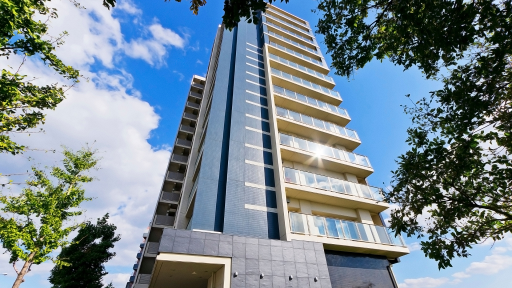 Ground view image of a high-rise apartment building on a partly cloudy day with surrounding trees