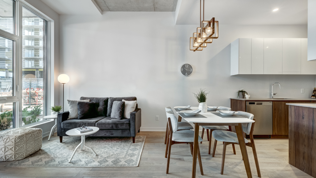 Wide shot image of a small furnished apartment with a light gray and wooden color palette