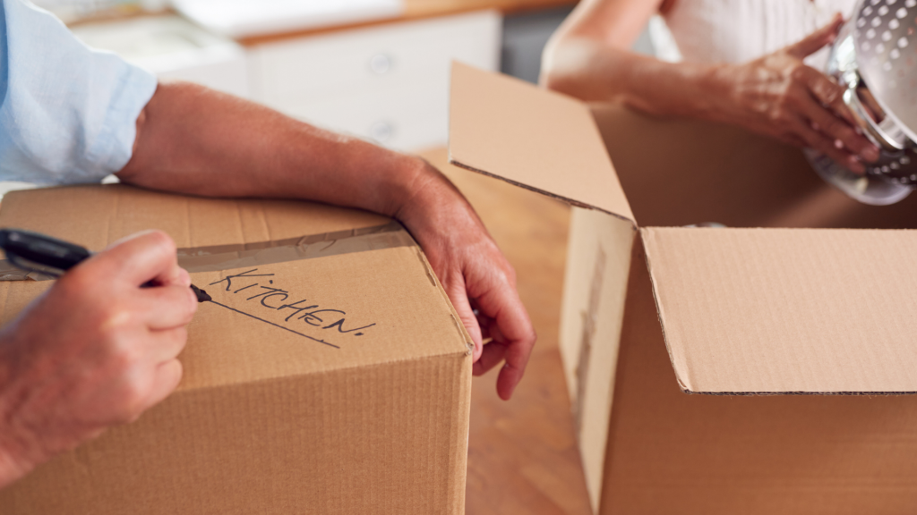 Closeup image of two people packing and labeling kitchen boxes for moving