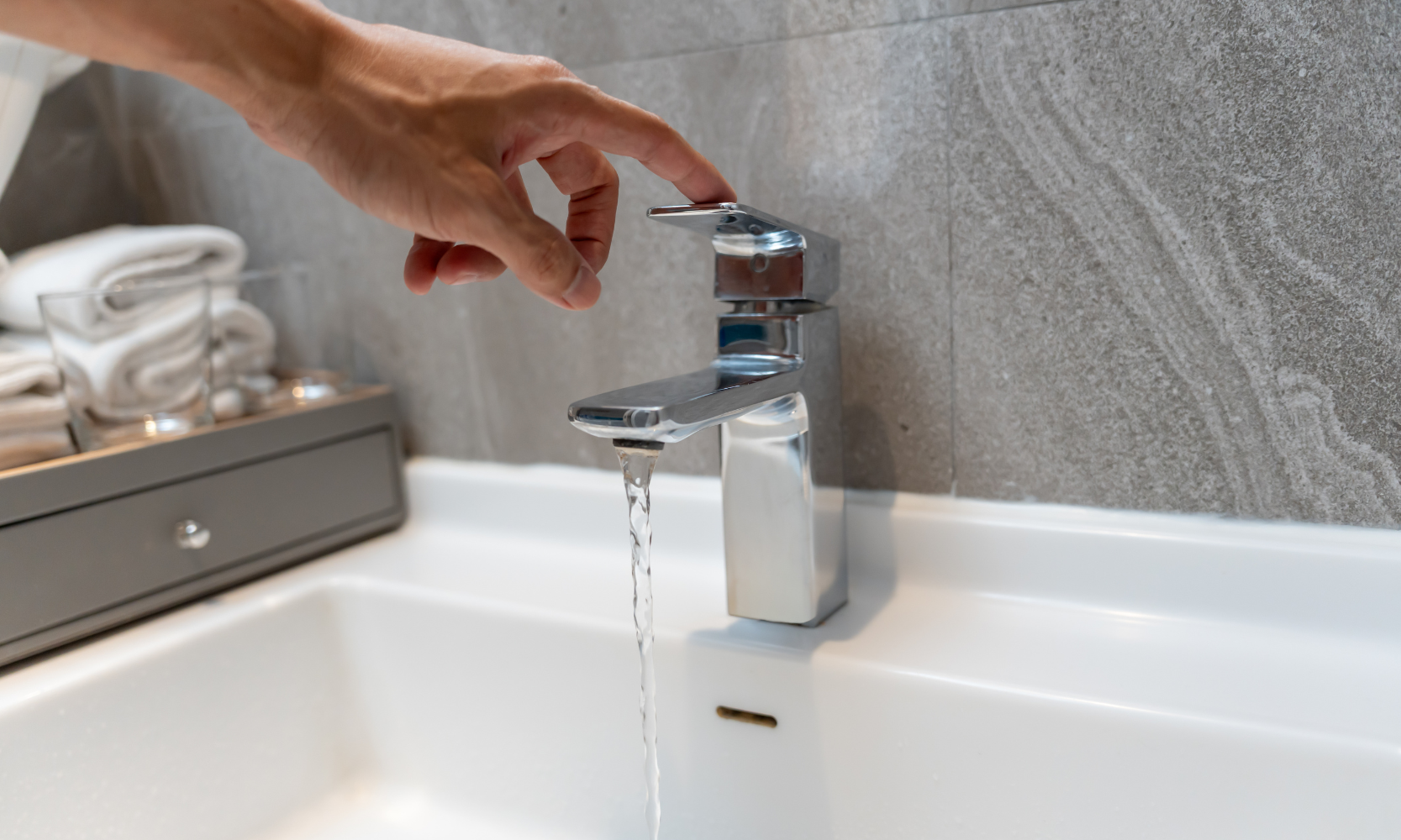 Close-up of a hand touching a sink water faucet that's on with water running