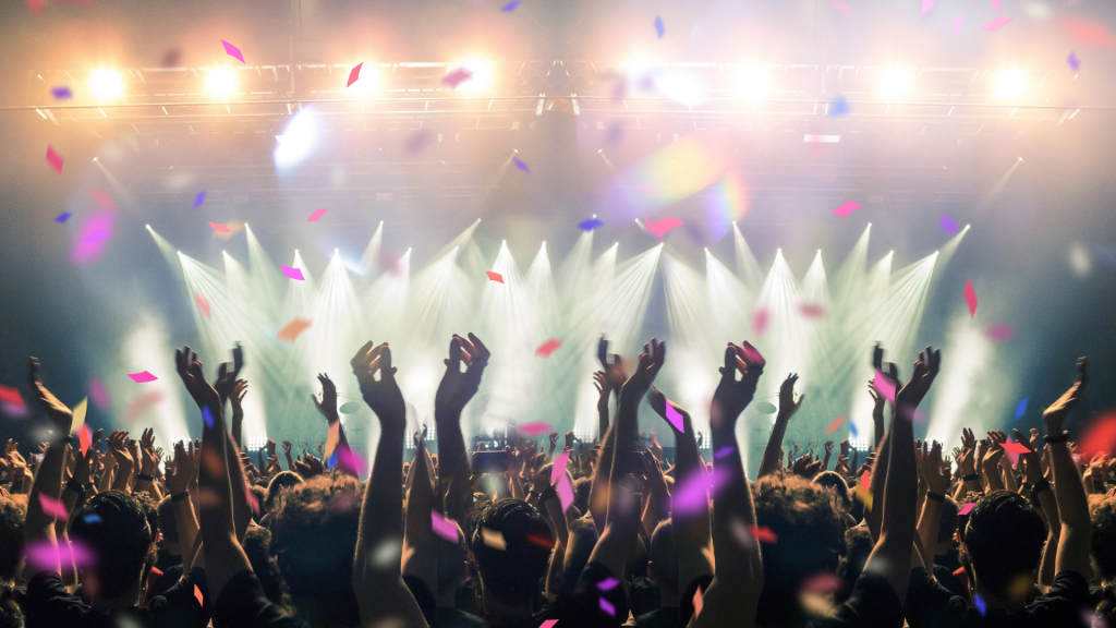 Rear-view image of a crowd dancing at a music festival with confetti and lights in the air